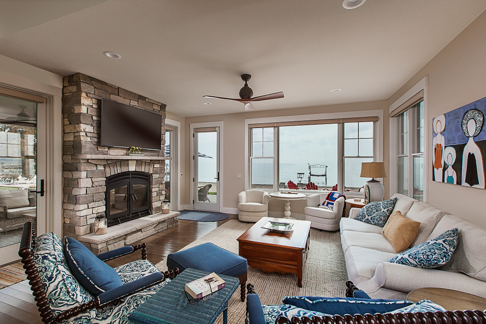 This is an example of a mid-sized beach style enclosed family room in Grand Rapids with a standard fireplace, a stone fireplace surround, a wall-mounted tv, beige walls and dark hardwood floors.