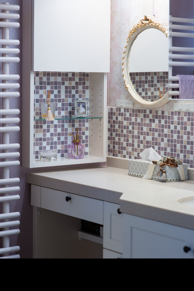 Design ideas for a small eclectic powder room with furniture-like cabinets, white cabinets, pink tile, glass tile, pink walls, vinyl floors, an undermount sink, solid surface benchtops and beige floor.