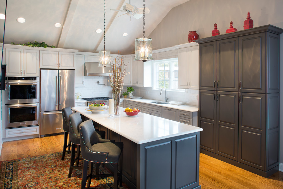 Inspiration for a mid-sized transitional l-shaped medium tone wood floor and brown floor eat-in kitchen remodel with an undermount sink, raised-panel cabinets, quartz countertops, white backsplash, subway tile backsplash, stainless steel appliances, an island and white countertops