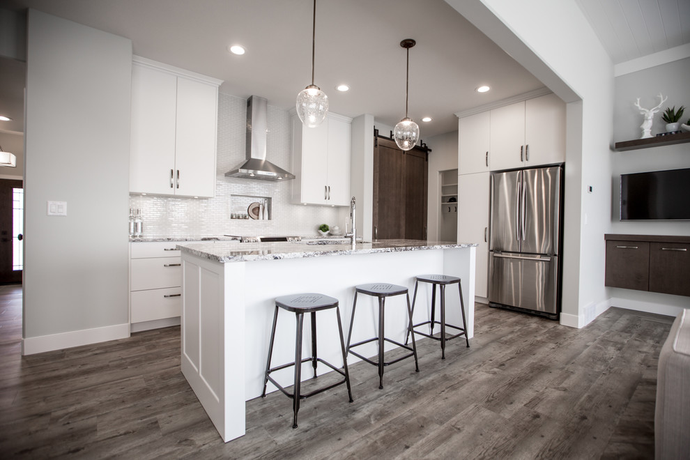 Mid-sized transitional l-shaped vinyl floor open concept kitchen photo with an undermount sink, flat-panel cabinets, white cabinets, granite countertops, gray backsplash, ceramic backsplash, stainless steel appliances and an island