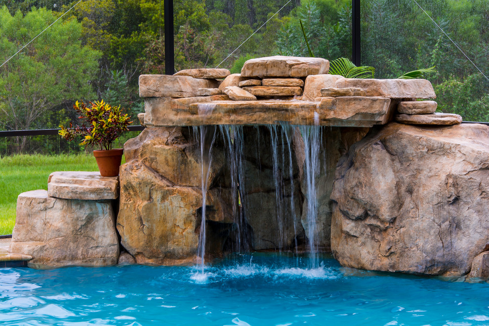 Inspiration for a large tropical backyard custom-shaped natural pool in Tampa with a water feature and natural stone pavers.
