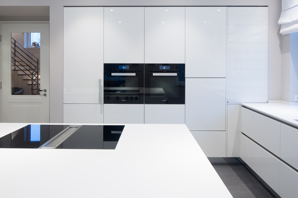 This is an example of a mid-sized scandinavian l-shaped separate kitchen in Hamburg with flat-panel cabinets, white cabinets, white splashback, with island, black appliances, an integrated sink and grey floor.