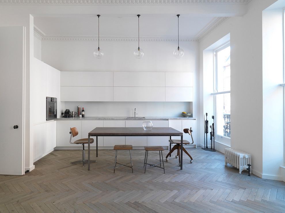 Photo of a scandinavian l-shaped eat-in kitchen in London with an undermount sink, flat-panel cabinets, white cabinets, light hardwood floors and no island.