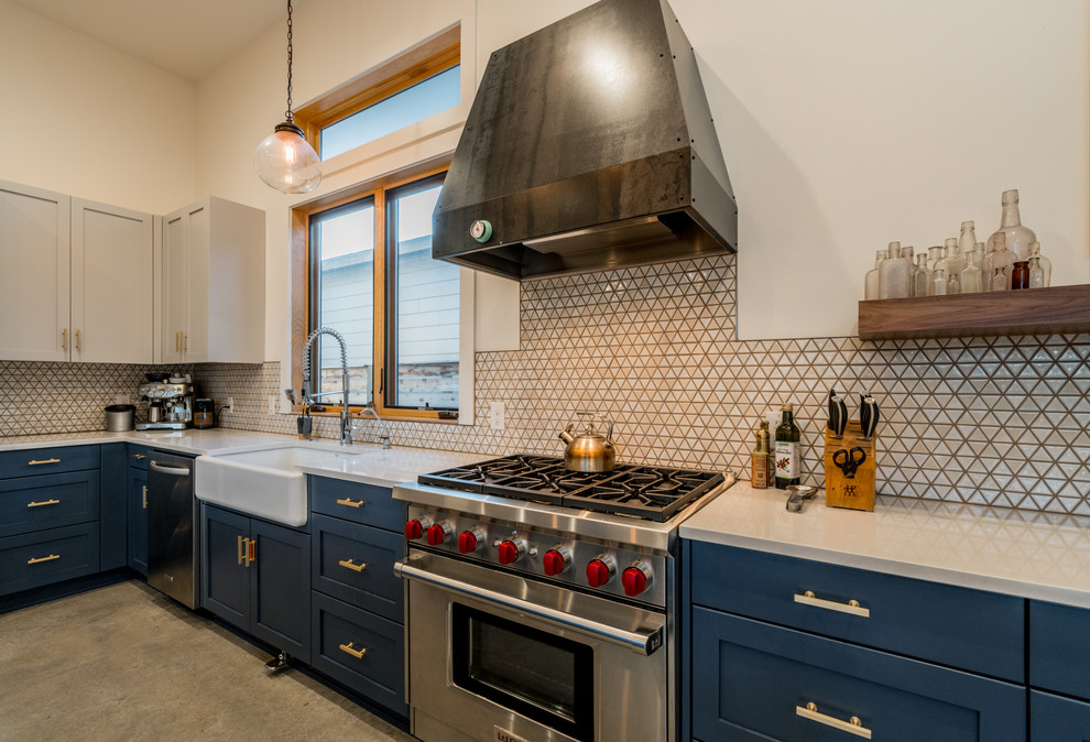 Design ideas for a transitional kitchen in Austin with a farmhouse sink, shaker cabinets, blue cabinets, beige splashback, stainless steel appliances and concrete floors.