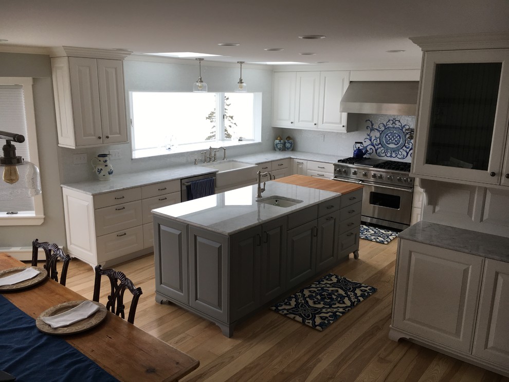 Design ideas for a mid-sized traditional u-shaped eat-in kitchen in Portland Maine with a farmhouse sink, raised-panel cabinets, white cabinets, marble benchtops, multi-coloured splashback, glass tile splashback, stainless steel appliances, light hardwood floors, with island and red floor.