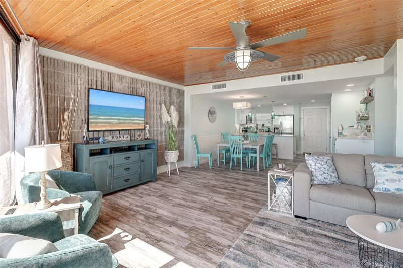 オースティンにある高級な中くらいなビーチスタイルのおしゃれなLDK (青い壁、磁器タイルの床、暖炉なし、壁掛け型テレビ、グレーの床、塗装板張りの天井) の写真