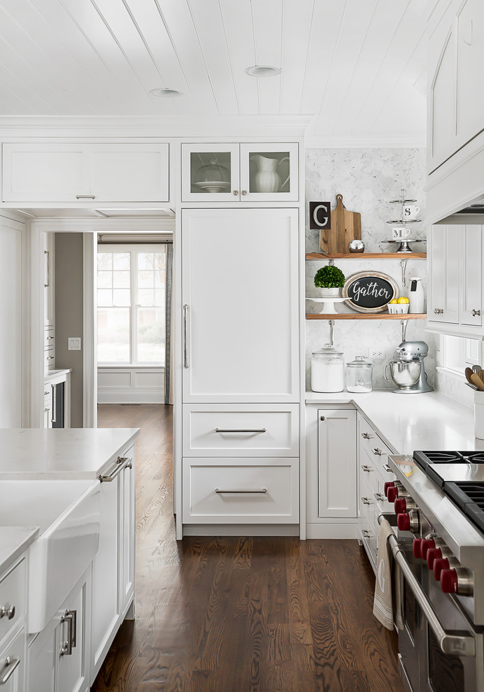 Inspiration for a large transitional eat-in kitchen in Chicago with a farmhouse sink, beaded inset cabinets, white cabinets, quartz benchtops, grey splashback, marble splashback, stainless steel appliances, medium hardwood floors, with island and brown floor.