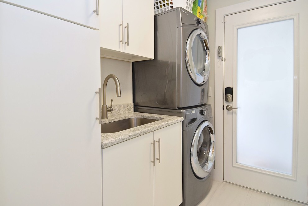 Inspiration for a small traditional single-wall dedicated laundry room in Tampa with an undermount sink, flat-panel cabinets, white cabinets, white walls, laminate floors, a stacked washer and dryer and white floor.