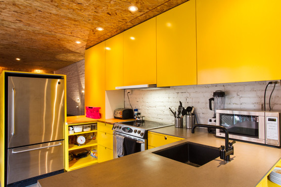 Modern kitchen in Montreal with yellow cabinets, white splashback and stainless steel appliances.