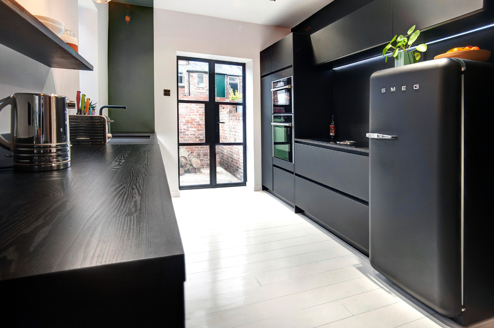 Photo of a small modern galley separate kitchen in Other with a single-bowl sink, flat-panel cabinets, black cabinets, quartzite benchtops, black splashback, black appliances, painted wood floors, no island, white floor, black benchtop and stone slab splashback.