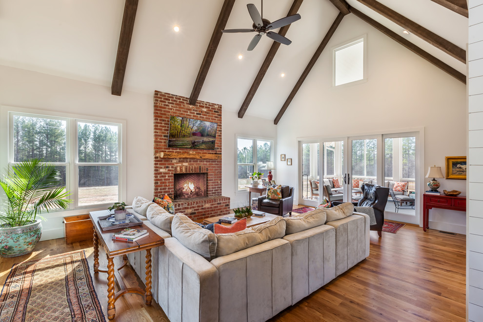 Design ideas for a large country open concept family room in Other with white walls, medium hardwood floors, a brick fireplace surround, a wall-mounted tv, brown floor and a standard fireplace.