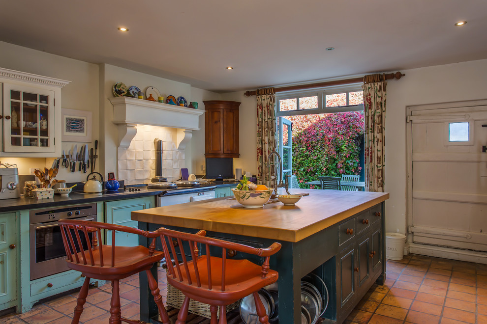 This is an example of a country kitchen in Sussex with recessed-panel cabinets, turquoise cabinets, white splashback, white appliances, terra-cotta floors and with island.
