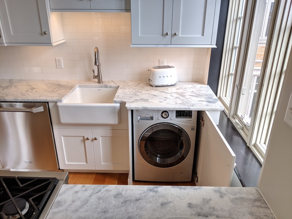 Photo of a small traditional galley eat-in kitchen in Other with a farmhouse sink, shaker cabinets, white cabinets, marble benchtops, white splashback, porcelain splashback, stainless steel appliances, medium hardwood floors, brown floor and white benchtop.