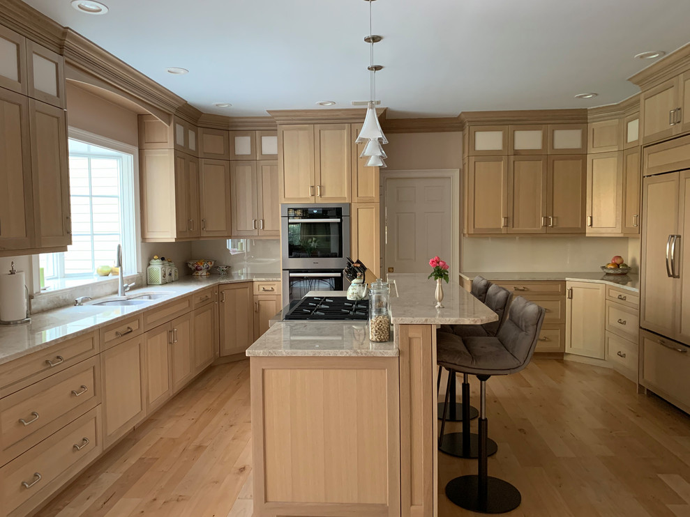 Large country eat-in kitchen in New York with a drop-in sink, shaker cabinets, beige cabinets, limestone benchtops, white splashback, cement tile splashback, stainless steel appliances, light hardwood floors, with island, beige floor and beige benchtop.