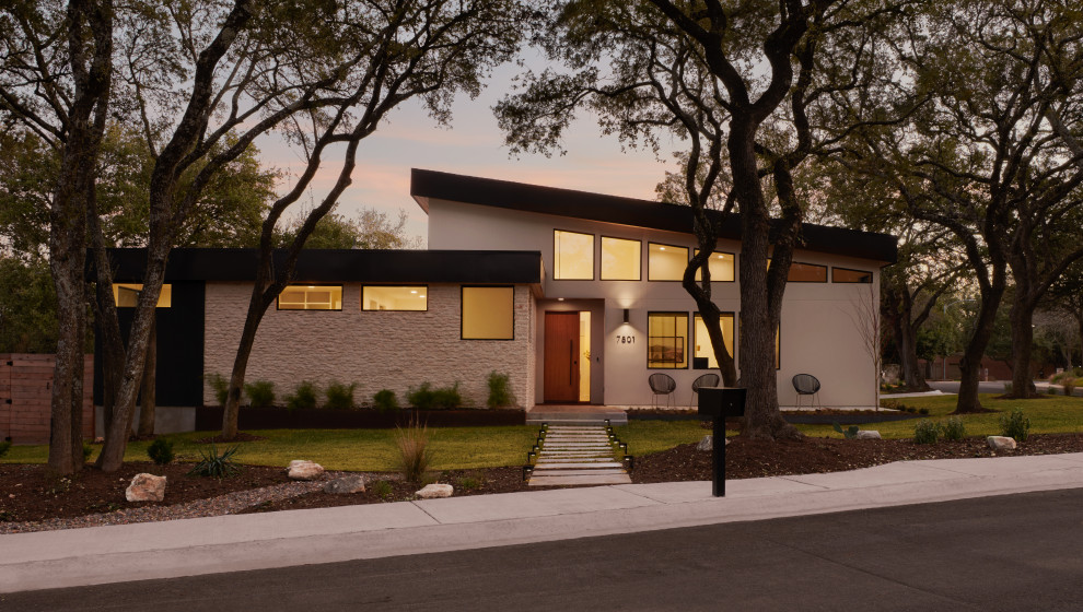 Photo of a large midcentury one-storey beige house exterior in Austin with mixed siding, a flat roof, a metal roof and a black roof.