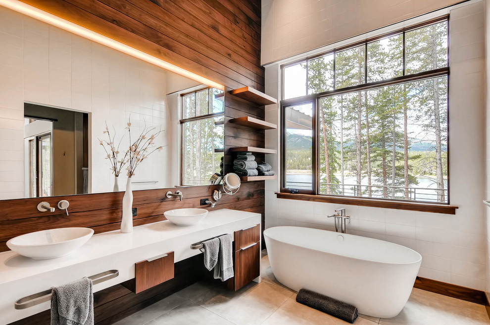 This is an example of a large contemporary master bathroom in Denver with flat-panel cabinets, white cabinets, a freestanding tub, white tile, brown walls, a vessel sink, beige floor and solid surface benchtops.