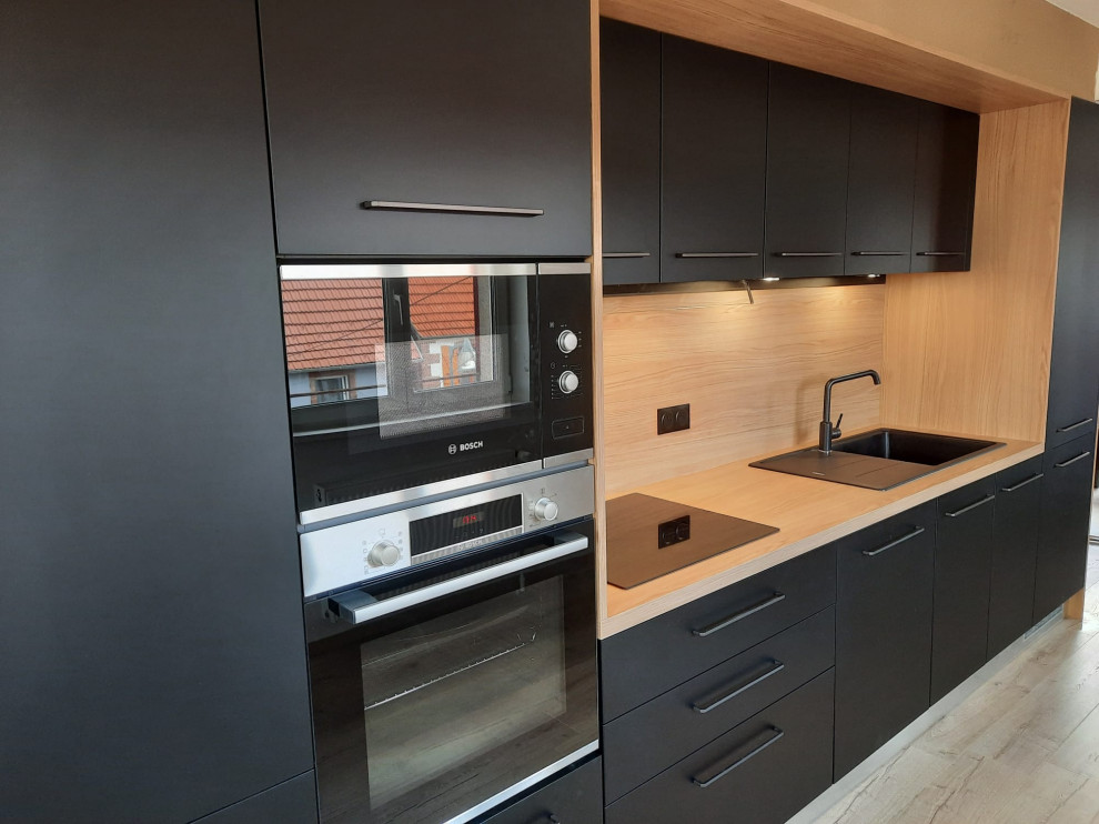 Idée de décoration pour une cuisine ouverte noire et bois design en L de taille moyenne avec un évier 1 bac, des portes de placard noires et un plan de travail en stratifié.