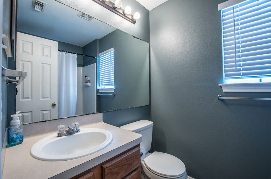 Photo of a small traditional master bathroom in Austin with furniture-like cabinets, medium wood cabinets, a corner tub, a shower/bathtub combo, a two-piece toilet, blue walls, a drop-in sink and laminate benchtops.