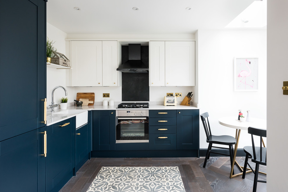 Mid-sized transitional l-shaped eat-in kitchen in London with a farmhouse sink, recessed-panel cabinets, blue cabinets, dark hardwood floors, brown floor and black appliances.