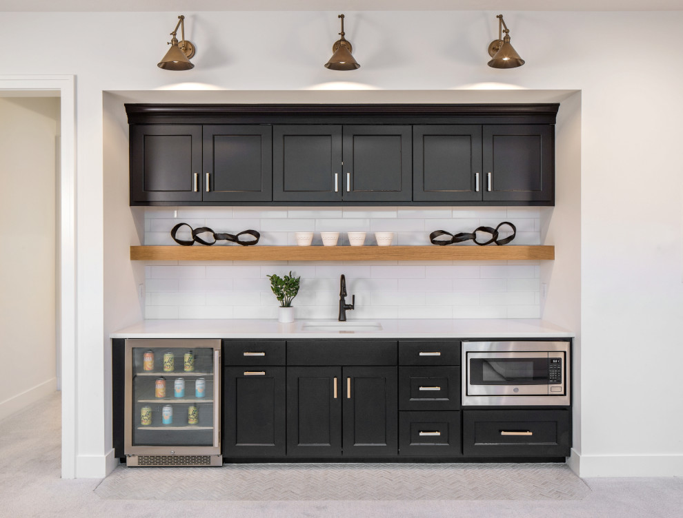 Design ideas for a mid-sized modern single-wall wet bar in Omaha with an undermount sink, shaker cabinets, black cabinets, quartz benchtops, white splashback, glass tile splashback, carpet, grey floor and white benchtop.