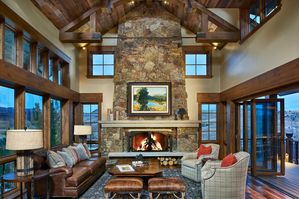 Design ideas for a country open concept family room in Denver with beige walls, dark hardwood floors, a standard fireplace, a stone fireplace surround and a concealed tv.