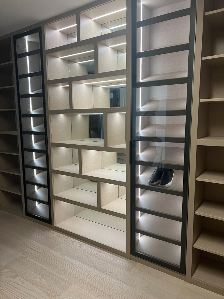 Photo of a large gender-neutral walk-in wardrobe in Miami with glass-front cabinets, white cabinets, light hardwood floors and beige floor.