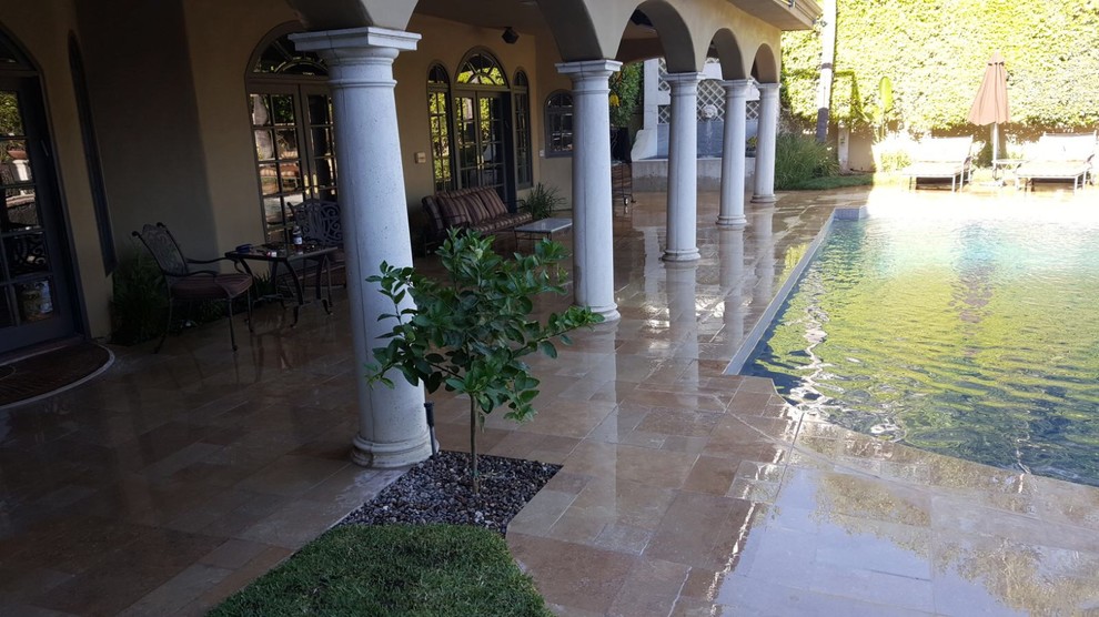 Photo of a large mediterranean backyard custom-shaped lap pool in Los Angeles with a water feature and natural stone pavers.