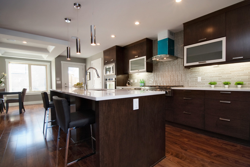 Photo of a large transitional single-wall eat-in kitchen in Calgary with flat-panel cabinets, dark wood cabinets, quartz benchtops, grey splashback, mosaic tile splashback, stainless steel appliances, medium hardwood floors, a drop-in sink and with island.