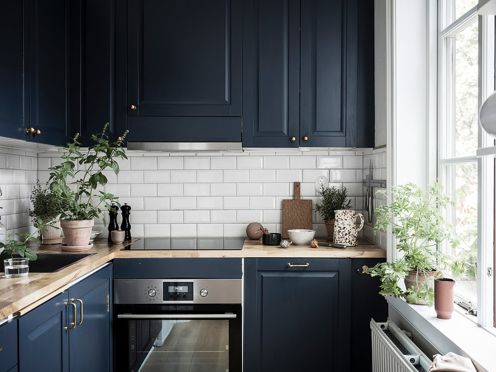 Small scandinavian l-shaped separate kitchen in Gothenburg with a single-bowl sink, raised-panel cabinets, blue cabinets, wood benchtops, white splashback, subway tile splashback, stainless steel appliances, no island and beige benchtop.
