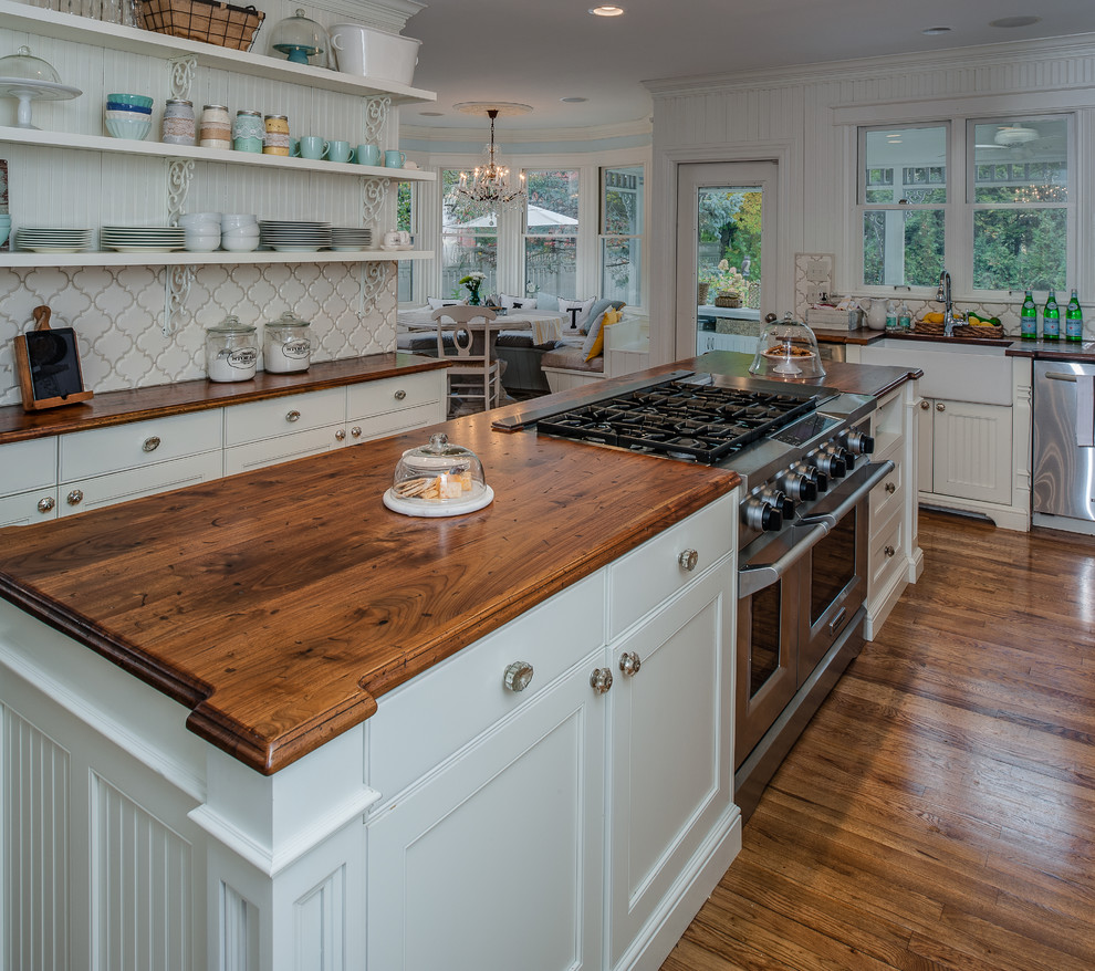 Photo of a large traditional l-shaped eat-in kitchen in Detroit with a farmhouse sink, shaker cabinets, white cabinets, wood benchtops, white splashback, ceramic splashback, white appliances, medium hardwood floors and with island.