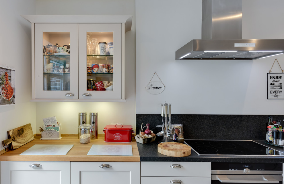 This is an example of a medium sized farmhouse galley kitchen/diner in Hamburg with a belfast sink, beaded cabinets, wood worktops, black splashback, marble splashback, stainless steel appliances, ceramic flooring, a breakfast bar, white cabinets and grey floors.