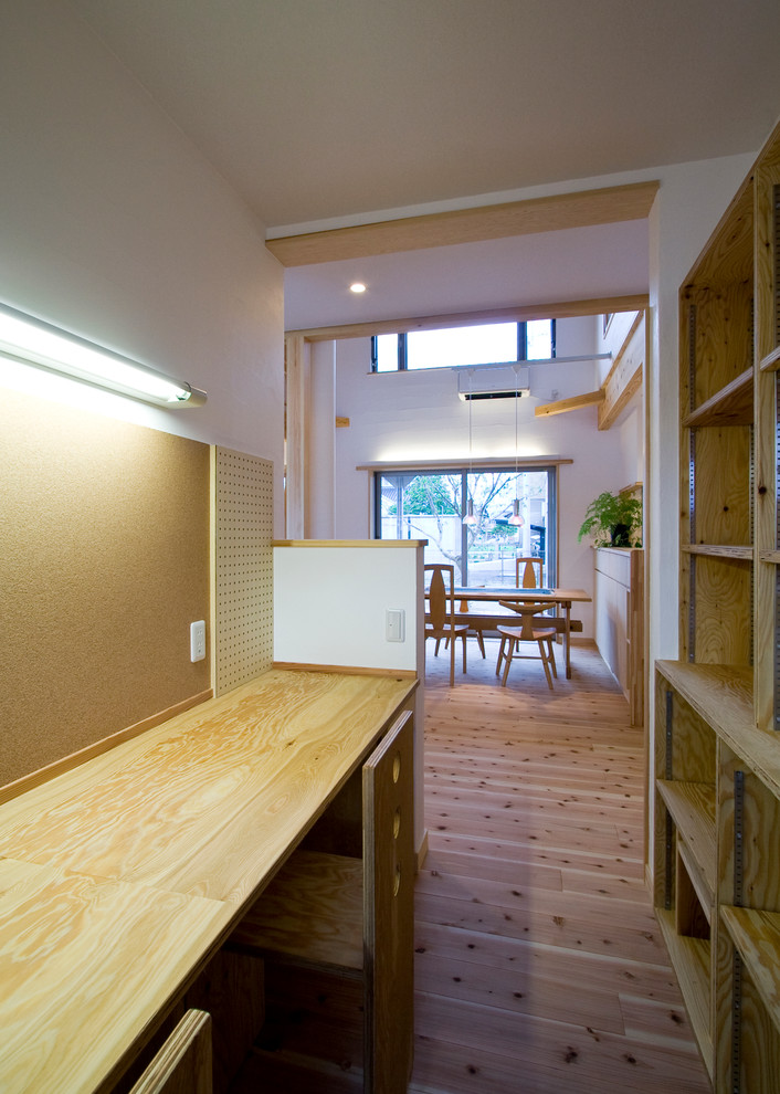 This is an example of a small modern home office in Other with white walls, light hardwood floors, a built-in desk and beige floor.
