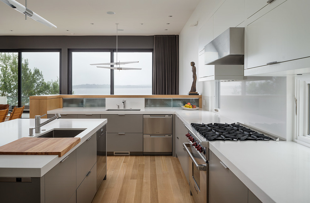Photo of a mid-sized modern u-shaped eat-in kitchen in Seattle with an undermount sink, flat-panel cabinets, grey cabinets, stainless steel appliances, quartz benchtops, white splashback, light hardwood floors and with island.