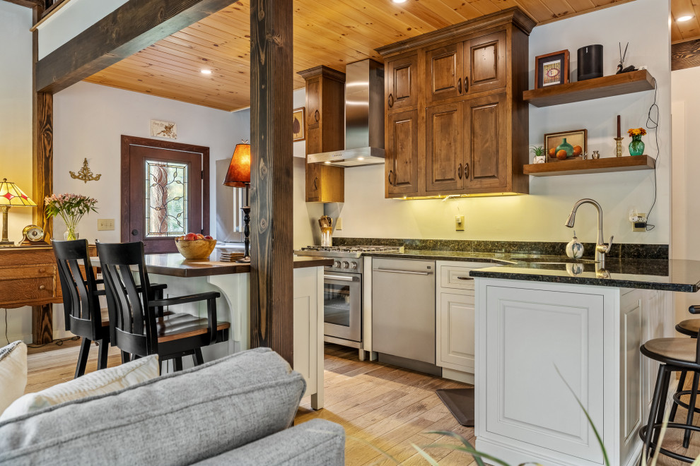 This is an example of a country l-shaped kitchen in Burlington with an undermount sink, raised-panel cabinets, white cabinets, medium hardwood floors, with island, brown floor and black benchtop.
