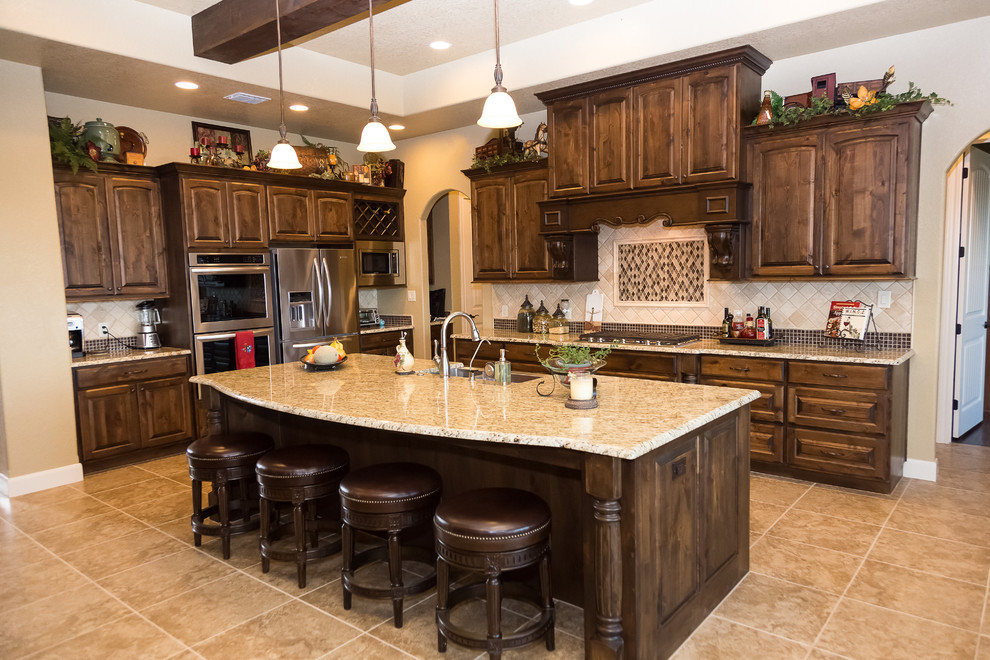 This is an example of a mid-sized arts and crafts l-shaped eat-in kitchen in Austin with a farmhouse sink, raised-panel cabinets, dark wood cabinets, granite benchtops, beige splashback, ceramic splashback, stainless steel appliances, travertine floors and with island.