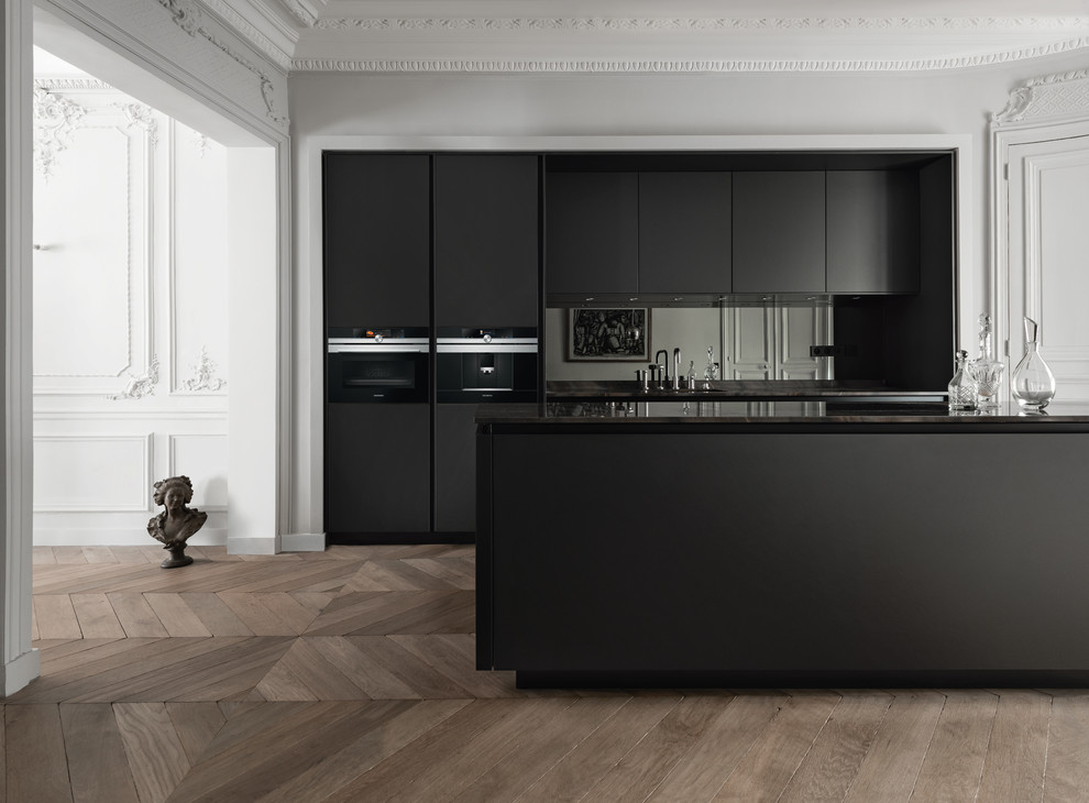 This is an example of a mid-sized contemporary single-wall eat-in kitchen in Paris with an undermount sink, flat-panel cabinets, black cabinets, black splashback, black appliances, medium hardwood floors and with island.