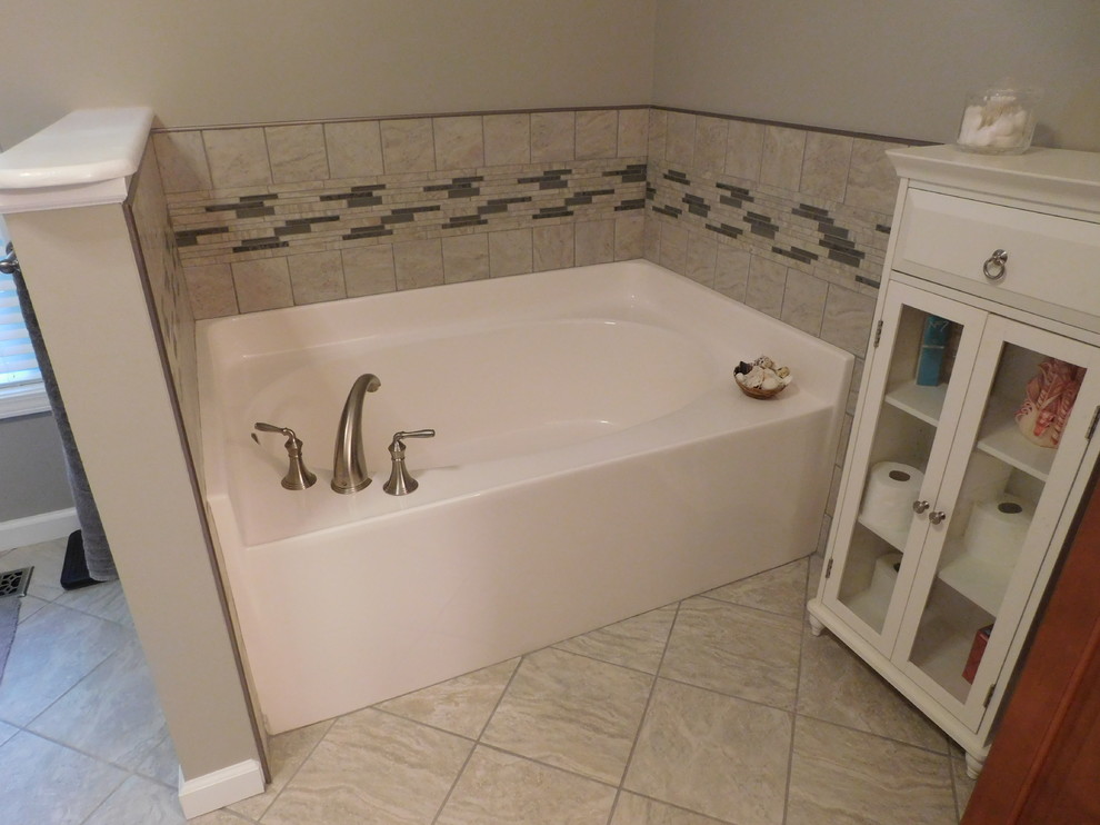 Example of a large transitional master gray tile and ceramic tile ceramic tile corner bathtub design with raised-panel cabinets, medium tone wood cabinets, a two-piece toilet, beige walls, an undermount sink and granite countertops