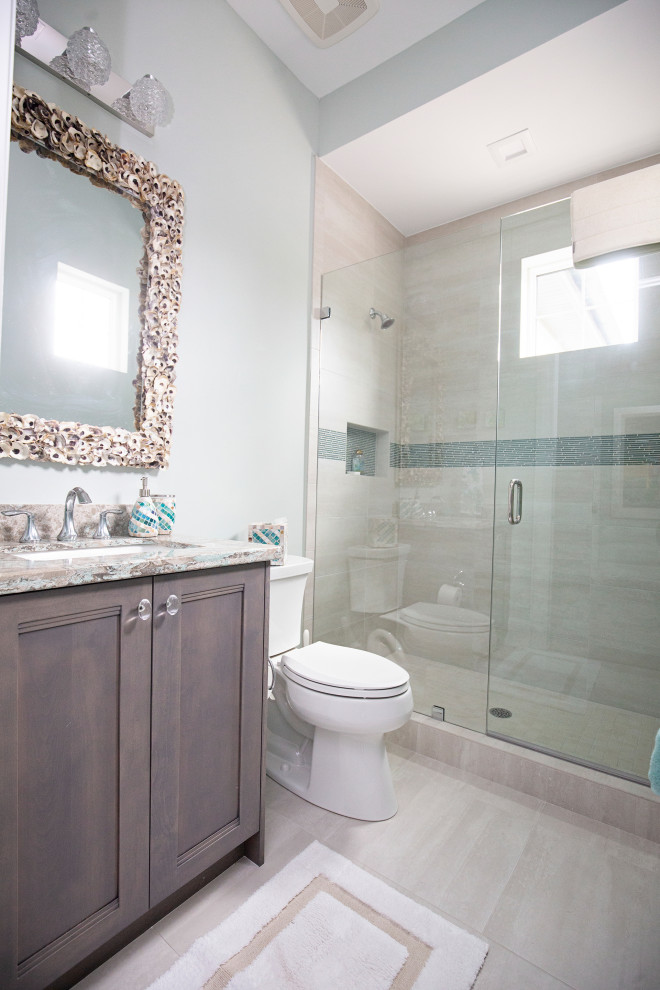 Photo of a mid-sized beach style 3/4 bathroom in Miami with flat-panel cabinets, brown cabinets, an alcove shower, a one-piece toilet, white walls, ceramic floors, a drop-in sink, marble benchtops, grey floor, a hinged shower door, beige benchtops, a single vanity and a built-in vanity.