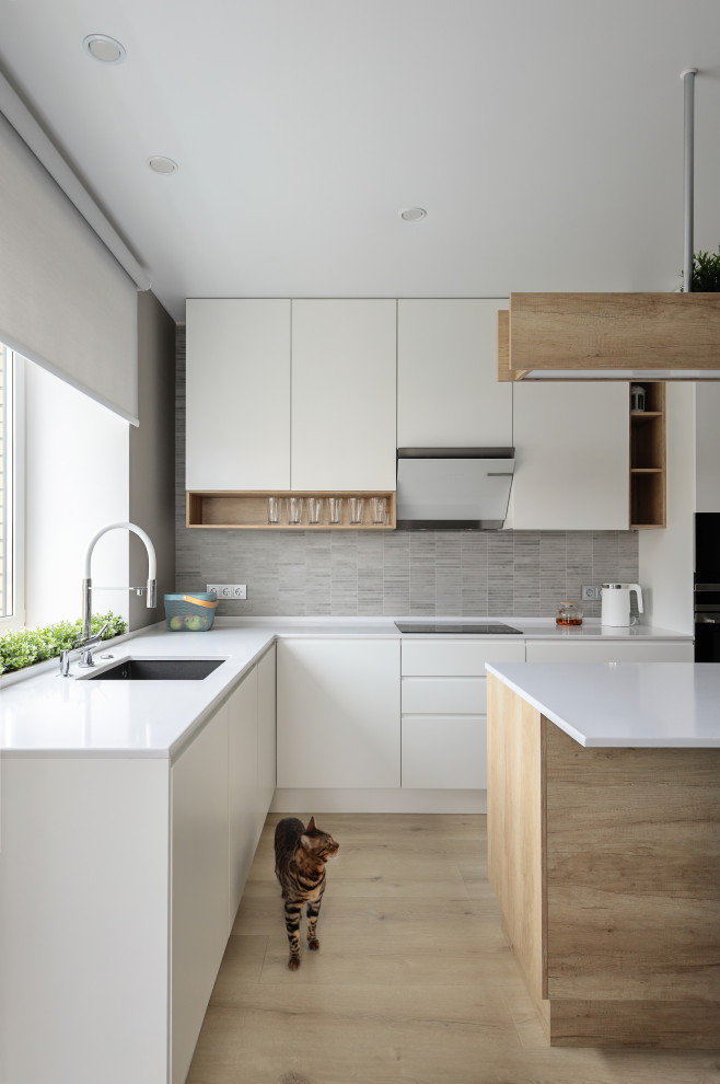 Design ideas for a mid-sized scandinavian u-shaped eat-in kitchen in Saint Petersburg with an undermount sink, flat-panel cabinets, white cabinets, solid surface benchtops, beige splashback, ceramic splashback, black appliances, medium hardwood floors, with island, brown floor and white benchtop.