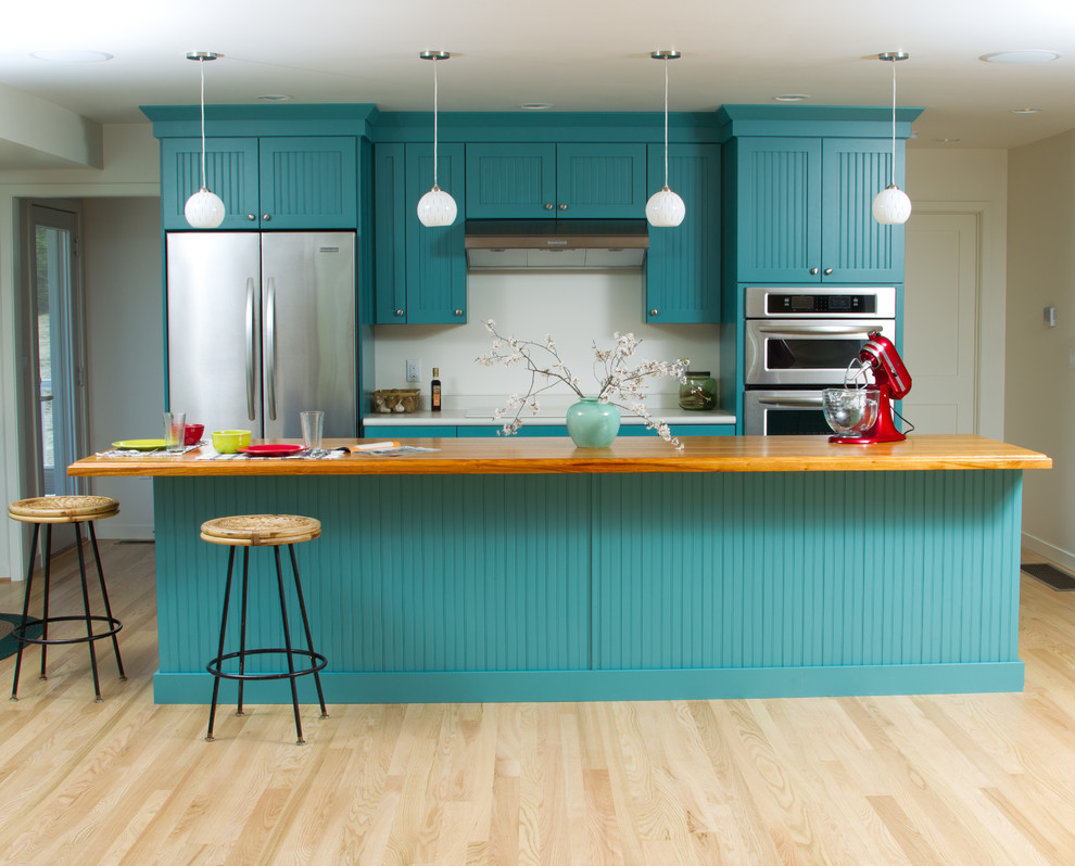 This is an example of a large arts and crafts galley eat-in kitchen in Minneapolis with shaker cabinets, blue cabinets, wood benchtops, white splashback, stainless steel appliances, light hardwood floors and with island.