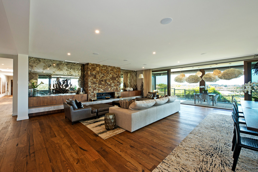 This is an example of a contemporary open concept living room in Melbourne with white walls, medium hardwood floors, a ribbon fireplace, a stone fireplace surround and brown floor.