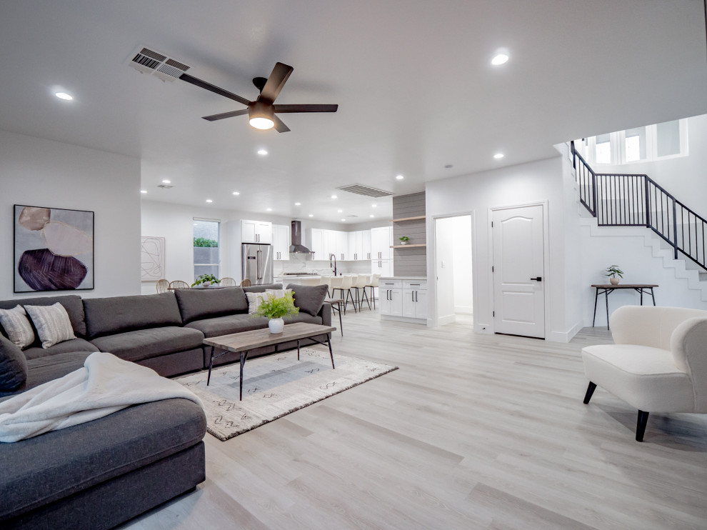 This is an example of a mid-sized modern open concept family room in Las Vegas with white walls, laminate floors, a standard fireplace and grey floor.
