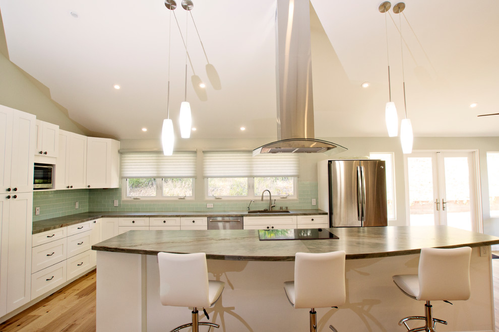 Photo of a mid-sized transitional l-shaped eat-in kitchen in San Diego with a drop-in sink, shaker cabinets, white cabinets, quartz benchtops, green splashback, glass tile splashback, stainless steel appliances, light hardwood floors, with island, brown floor and green benchtop.