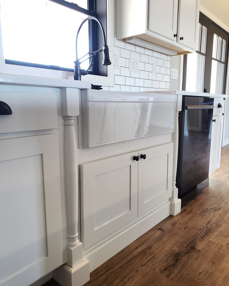 This is an example of a mid-sized country l-shaped eat-in kitchen in Kansas City with a farmhouse sink, flat-panel cabinets, white cabinets, quartz benchtops, white splashback, subway tile splashback, stainless steel appliances, vinyl floors, with island, grey floor and white benchtop.