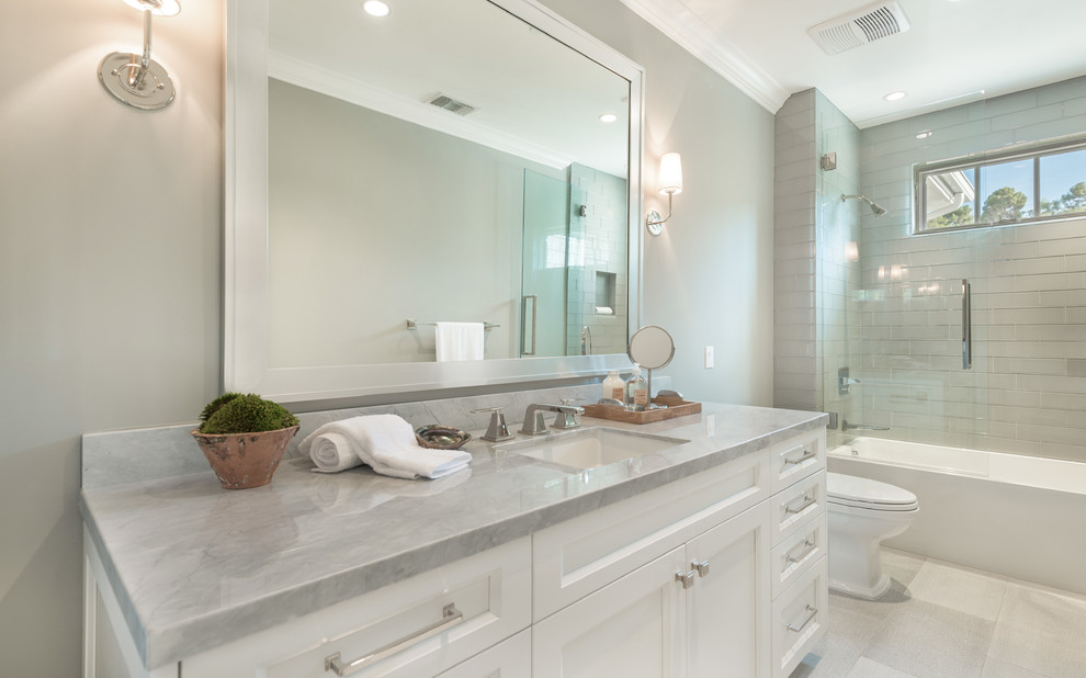 Design ideas for a mid-sized transitional kids bathroom in Los Angeles with recessed-panel cabinets, white cabinets, an alcove tub, an alcove shower, a one-piece toilet, gray tile, glass tile, grey walls, marble floors, an undermount sink and marble benchtops.