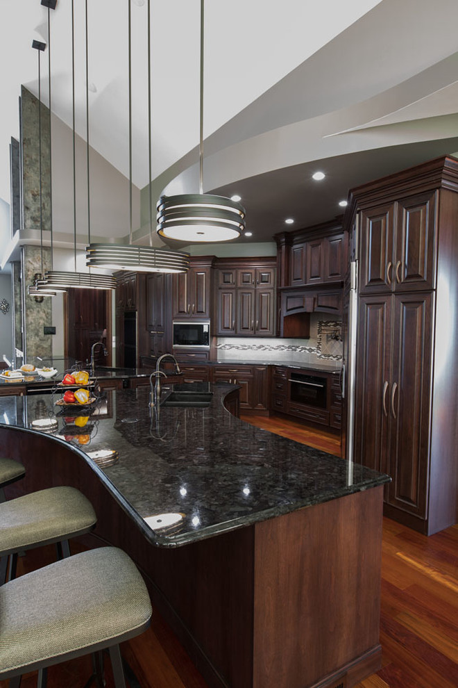 Inspiration for a transitional single-wall medium tone wood floor and brown floor eat-in kitchen remodel with an undermount sink, raised-panel cabinets, dark wood cabinets, granite countertops, black appliances, two islands and black countertops