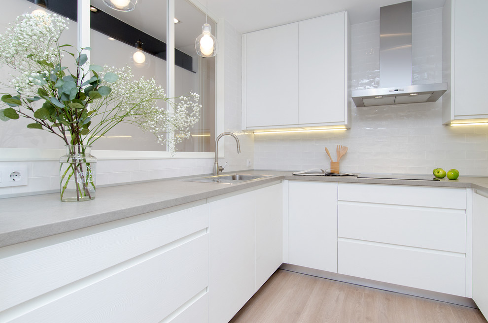 Inspiration for a mid-sized contemporary u-shaped open plan kitchen in Madrid with a single-bowl sink, raised-panel cabinets, white cabinets, concrete benchtops, white splashback, ceramic splashback, white appliances, light hardwood floors and no island.
