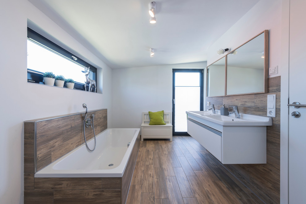 Inspiration for a mid-sized contemporary master bathroom in Other with flat-panel cabinets, white cabinets, a drop-in tub, a shower/bathtub combo, white walls, medium hardwood floors and an integrated sink.