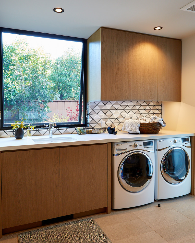 Photo of a contemporary single-wall dedicated laundry room in San Francisco with an undermount sink, flat-panel cabinets, medium wood cabinets, beige walls, a side-by-side washer and dryer, beige floor and white benchtop.