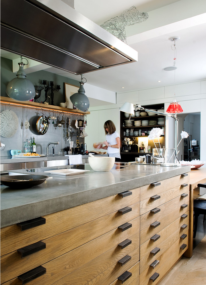 Example of a mid-sized urban light wood floor open concept kitchen design in Edinburgh with a farmhouse sink, flat-panel cabinets, medium tone wood cabinets, concrete countertops, gray backsplash, stainless steel appliances and an island